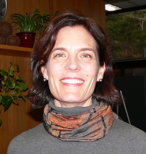 Sara Curran headshot in gray sweater, orange and gray scarf, short dark brown hair and smiling.