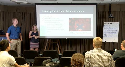 Two students giving a presentation with the projected slide titled "A new option for heart failure treatment".