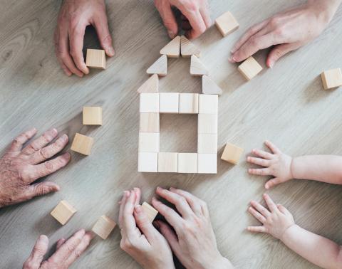 Multi-generational hands using wooden blocks to build the outline of a house.
