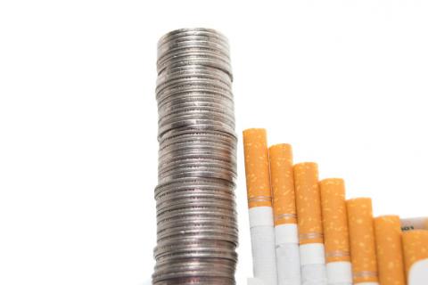 Photo of several cigarettes next to a large stack of coins.