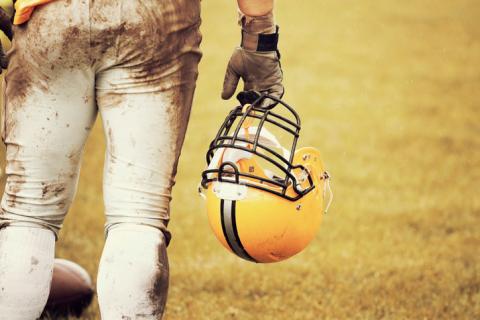 Photo of a muddied football player holding their helmet.