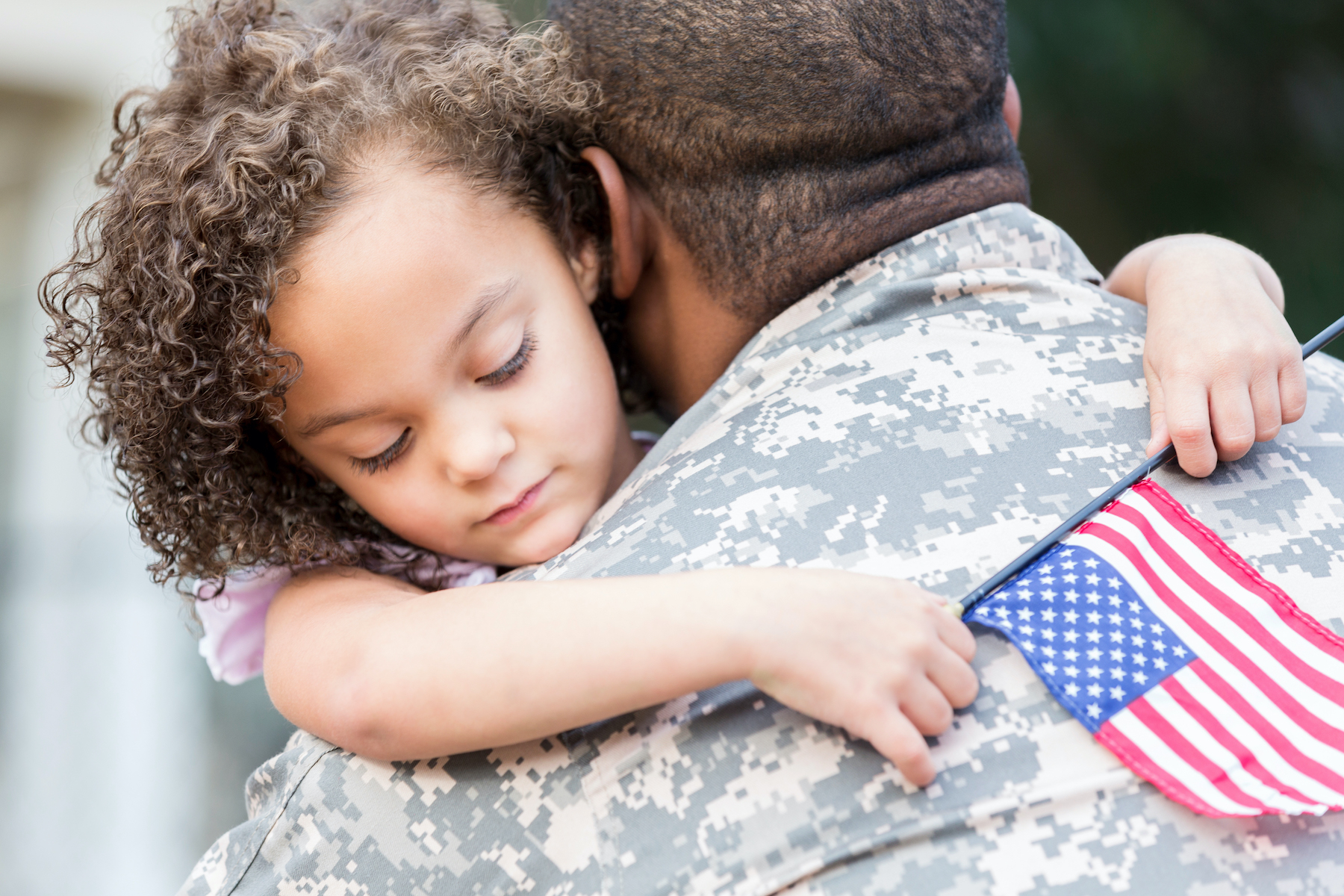 Military dad and small daughter hugging with flag.