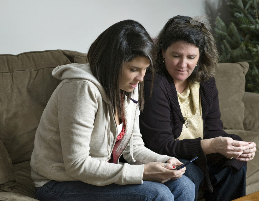 Mom and teen girl sitting on couch and talking over a cell phone.