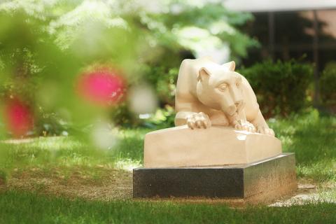 The Nittany Lion Shrine surrounded by green grass and a blurred tree branch in the foreground.
