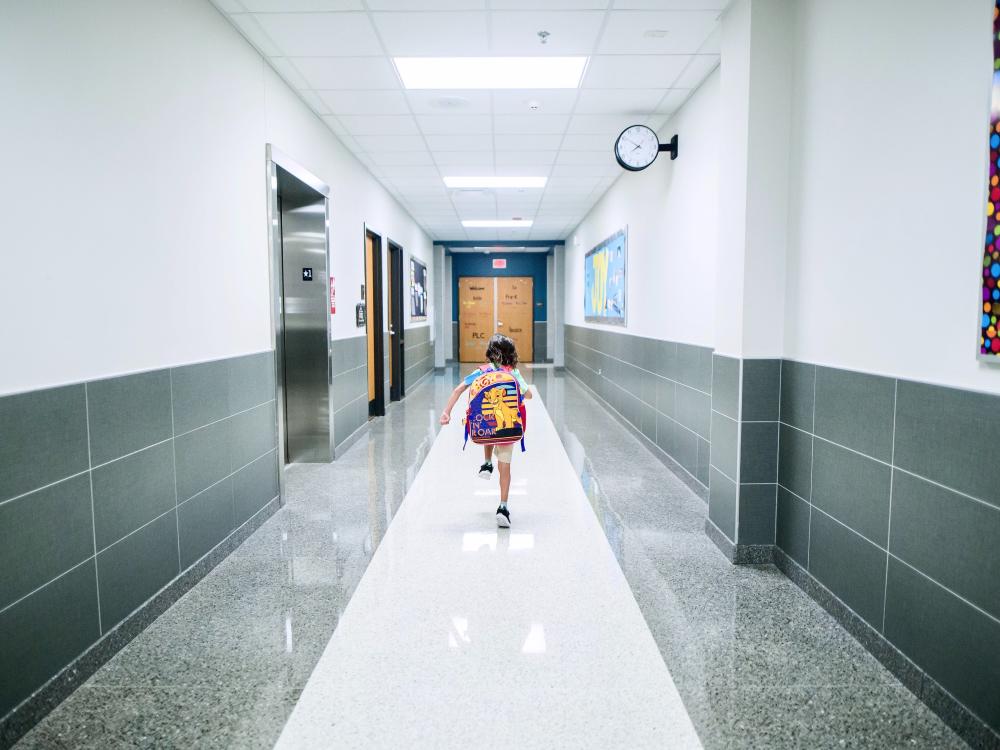 Child running through school hallway with backpack.