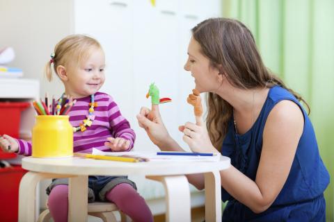 Photo of a woman playing with finger puppets with a toddler.