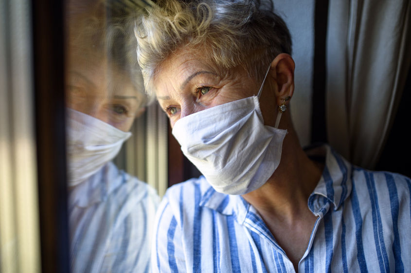 Senior woman with mask and blue shirt looking out window
