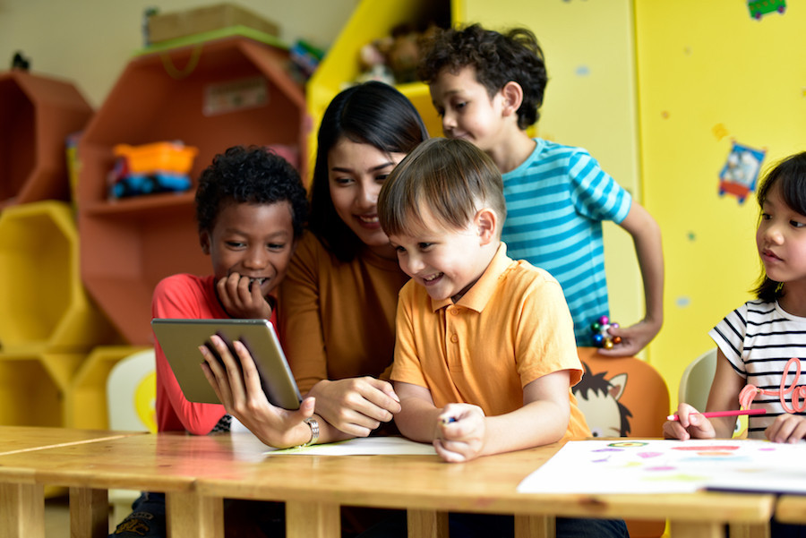 Young children and teacher gathered around an iPad.