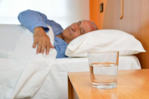 A man asleep in bed, with a glass of water on the nightstand beside him.
