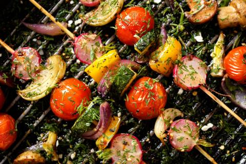 Skewered vegetables on a grill covered in seasoning.