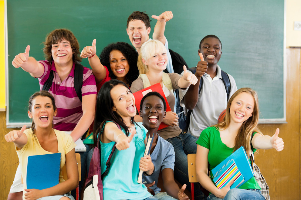 A group of teenage students posing in front of a classroom and giving a thumbs up.
