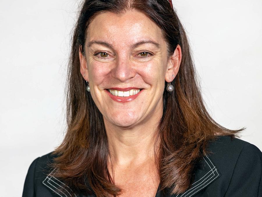 Janet Van Hell headshot, smiling, with long brown hair and black jacket.