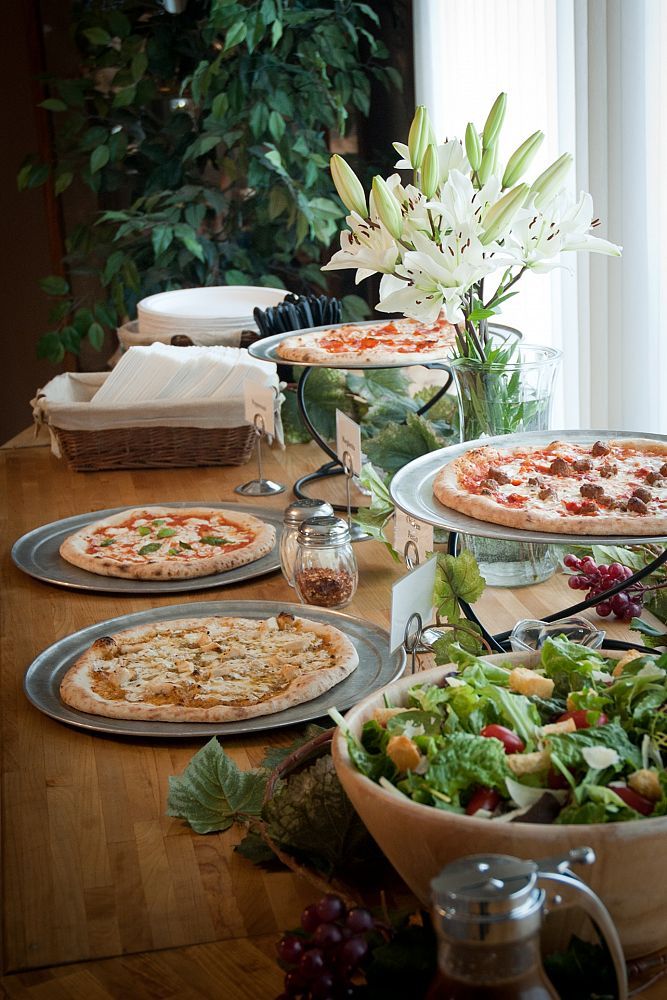 A buffet table set with various pizzas, salad, flowers, napkins, plates, and utensils.