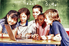 Photo of children gathered around their teacher and a laptop.