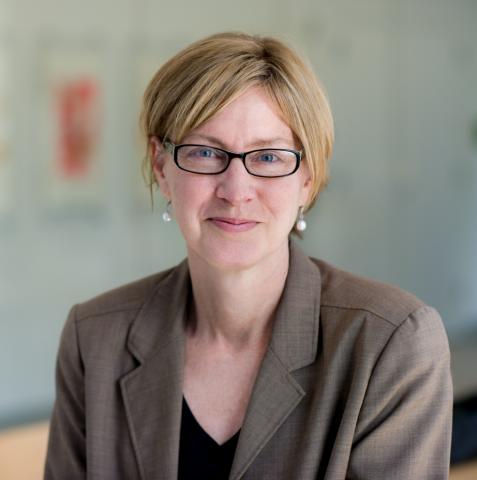 Photo of Susan Short with short blond hair, wearing black rimmed glasses, white pearl earrings, and a brown blazer. (From her bio on Brown University's website.)