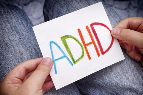 A child holding a piece of paper with the colorful letters "ADHD" written on it.