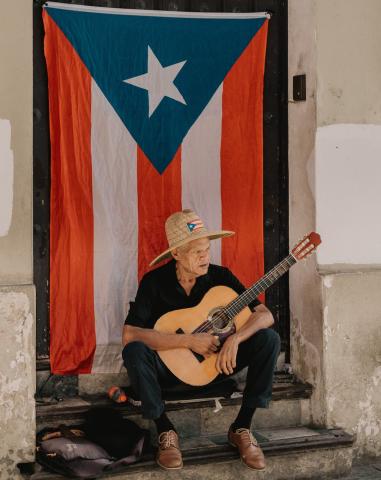 Puerto Rican man playing a guitar in front of flag.