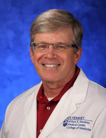 Headshot of Kent Hymel with gray hair, glasses, red shirt, and white coat.