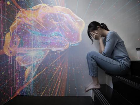 Woman sitting with face in hands and image of brain activity in background.