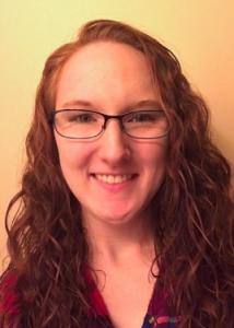 Headshot of Chelsea Dickens with long red hair, glasses, and red top.