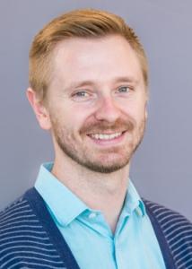 Headshot of Eric Layland with blonde hair, beard, light blue shirt, and blue and white striped sweater.