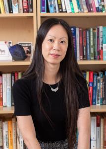 Jessica Ho headshot in black short sleeve shirt, long black hair in front of shelves of books.