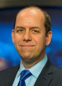 Headshot of John Gastil, a white man with a balding hairline wearing a black suit jacket and blue tie and shirt.