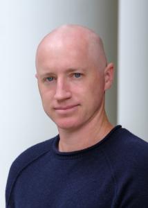 Headshot of Jonathan Wright with no hair and dark blue sweater.
