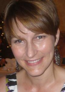 Headshot of Suzy Scherf with short brown hair, long silver earrings, and black and white patterned top.