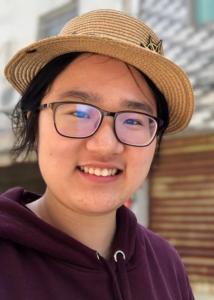 Headshot of Xiaoyue Xiong, with black har in straw hat and purple sweatshirt.