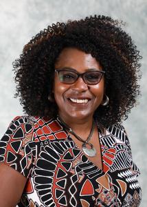 Headshot of Lynette Yarger, a black woman with curly hair and glasses wearing a short-sleeved black, red, and white patterned shirt.