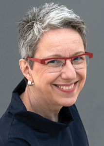 Headshot of Alexandra Staub, a white woman with short grey-white hair, red glasses, and a black shirt.