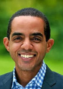 black male with short black hair, wearing a gingham blue shirt and black blazer