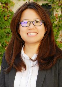 Headshot of Qi Li, an Asian woman with long brown hair, a black jacket, white shirt and glasses.