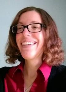 Headshot of Roseann McManus with short, curly brown hair, pink shirt, and black sweater with black plastic-frame glasses.
