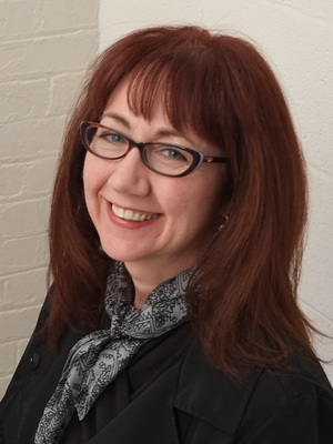Headshot of Kristi Williams with red hair, glasses, black top, and gray scarf.